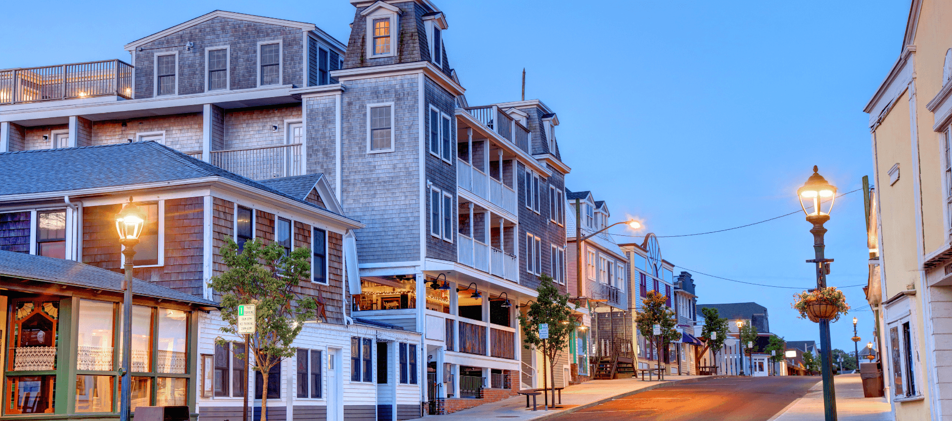 A quiet street lined with multi-story buildings and street lamps during twilight.