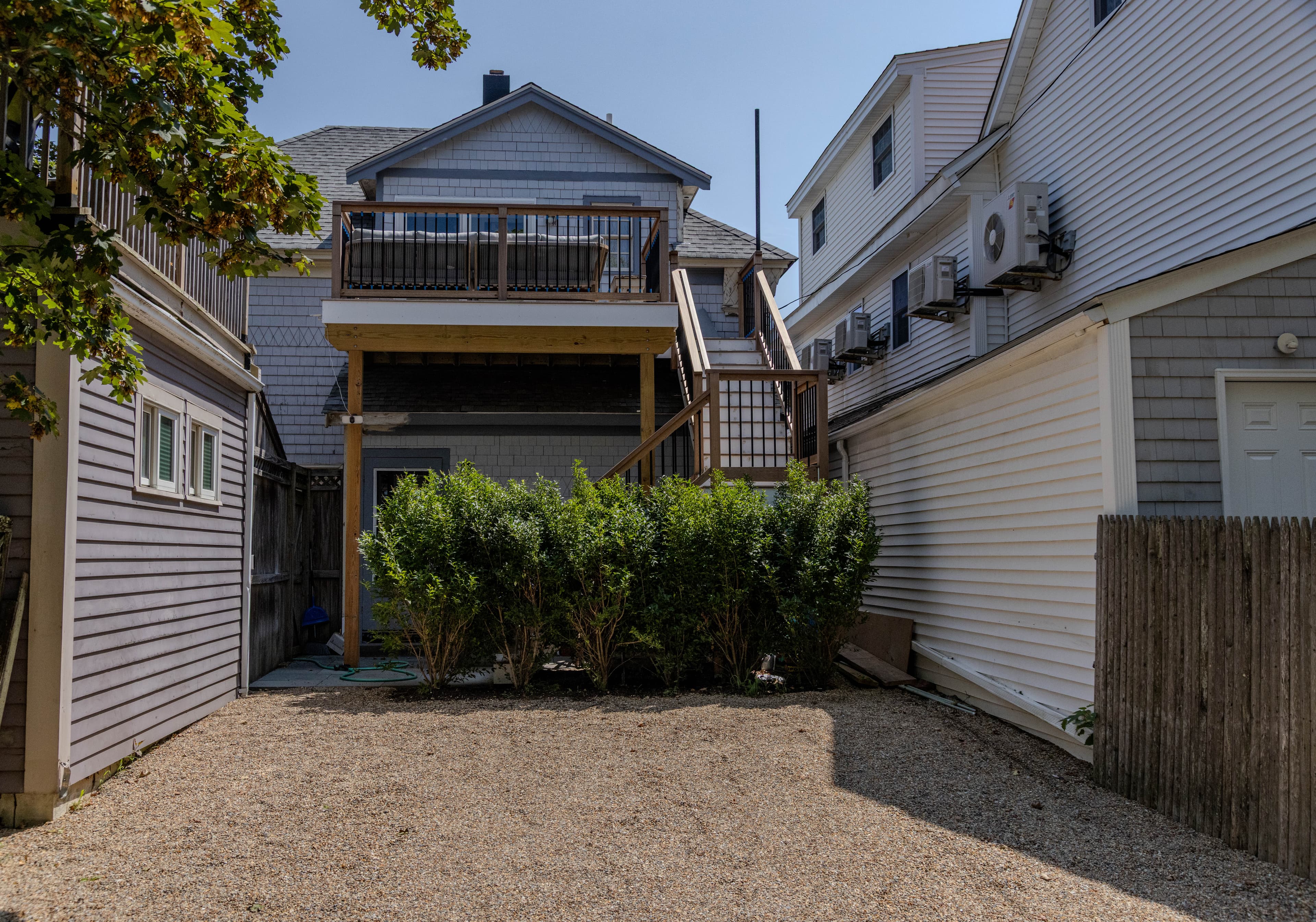 A small gravel yard with green shrubs and a two-story house featuring a balcony.