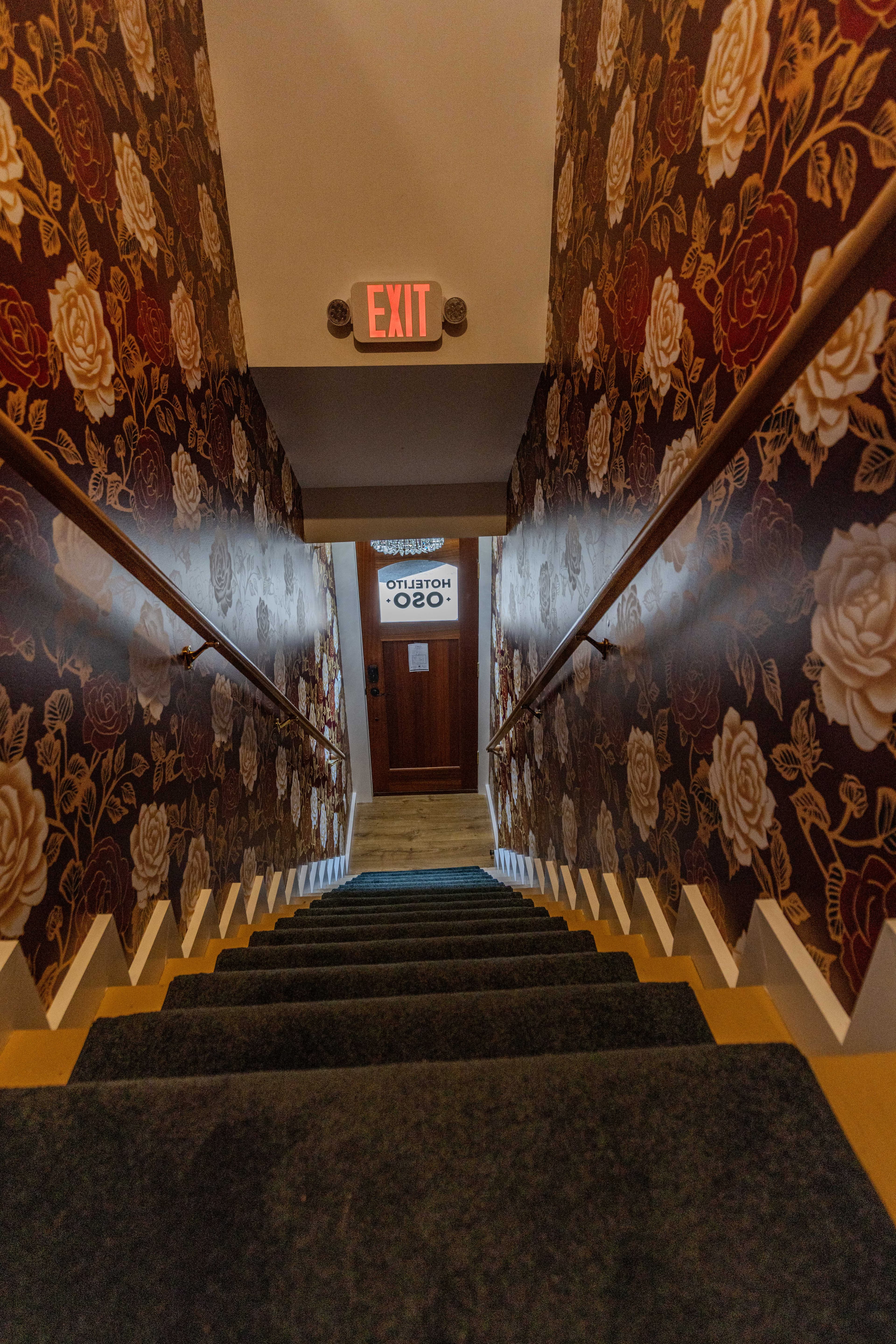 View down a staircase with floral wallpaper leading to a door marked "HOTEL."