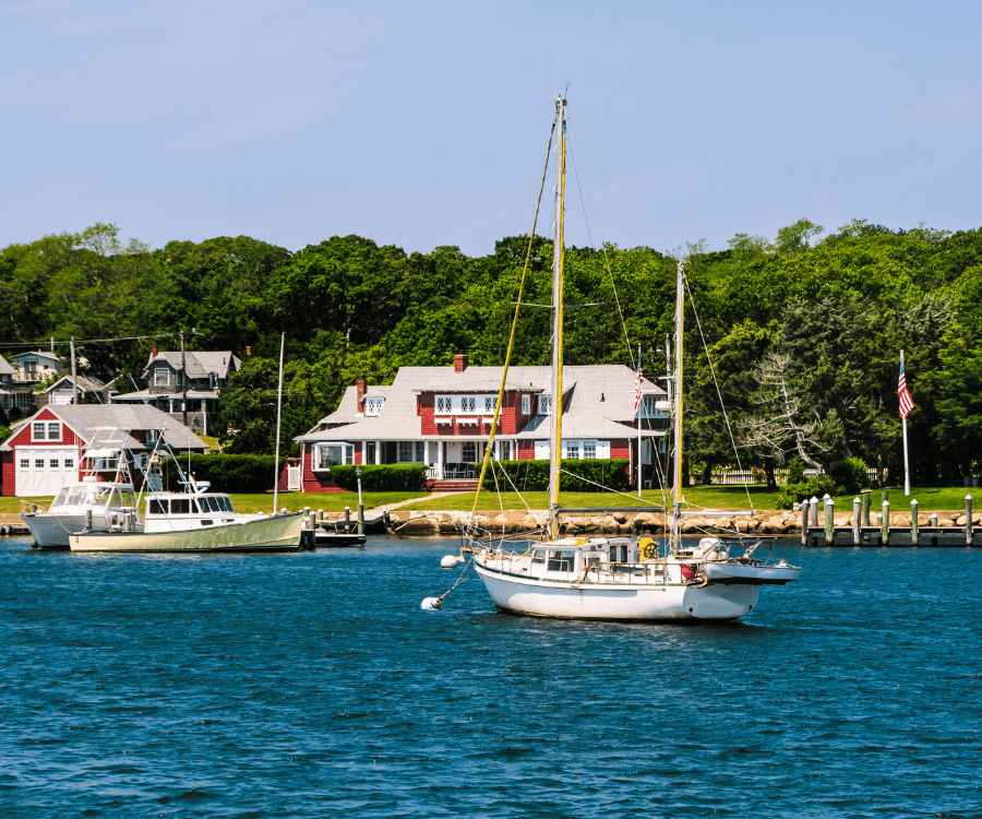 Sailboats anchored in a tranquil harbor with lush greenery and homes in the background.