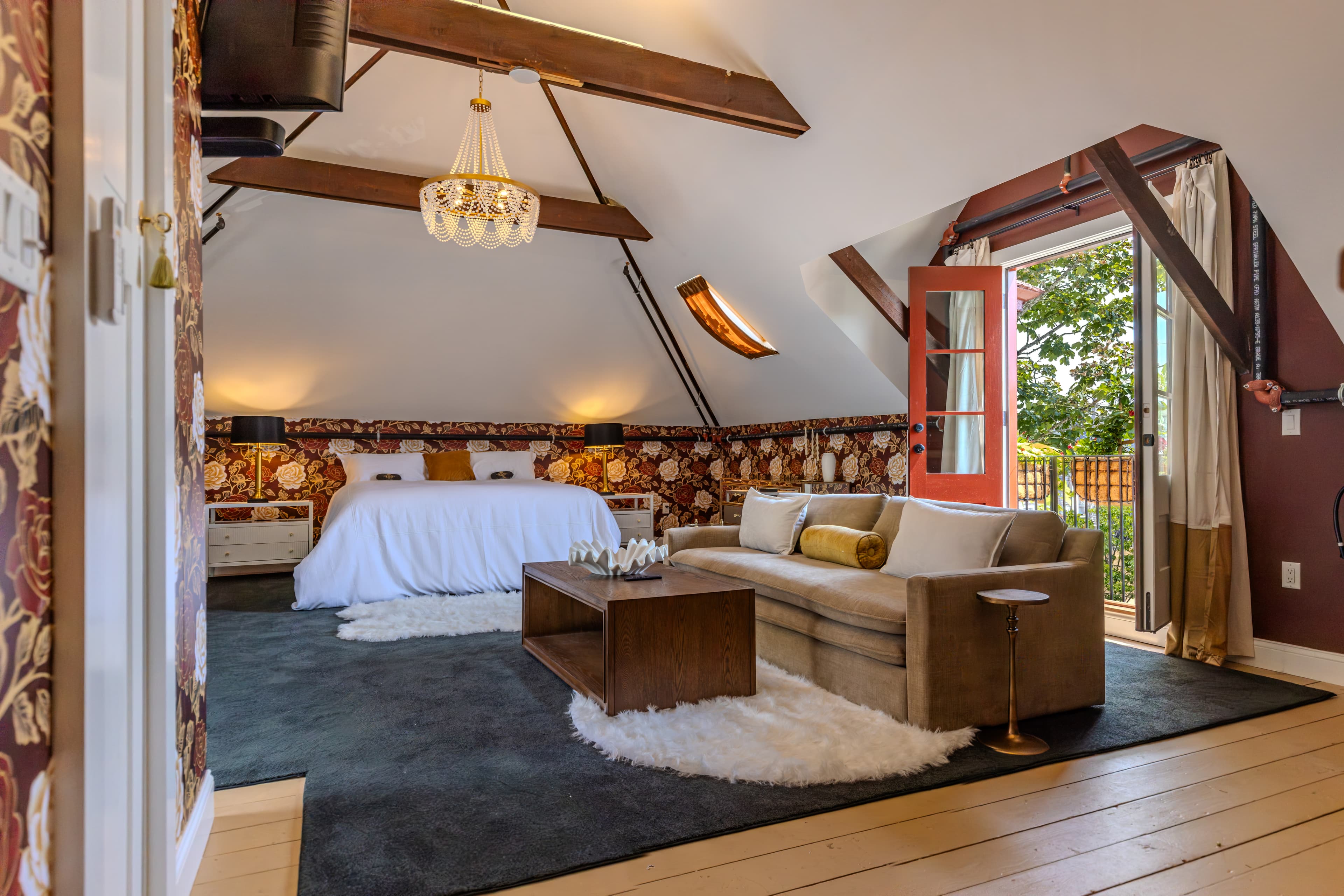 Cozy attic bedroom featuring a chandelier, a large bed, a sofa, and a view through open doors.