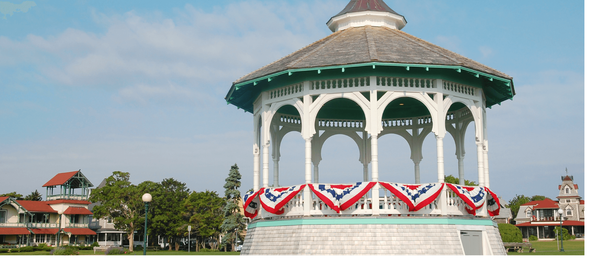 A decorative gazebo adorned with red, white, and blue bunting, surrounded by greenery and historic buildings.