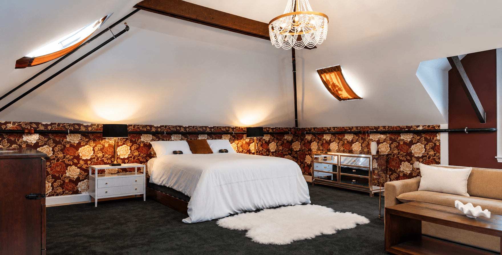 A cozy attic bedroom featuring a large bed, floral wallpaper, soft carpet, and modern furnishings.