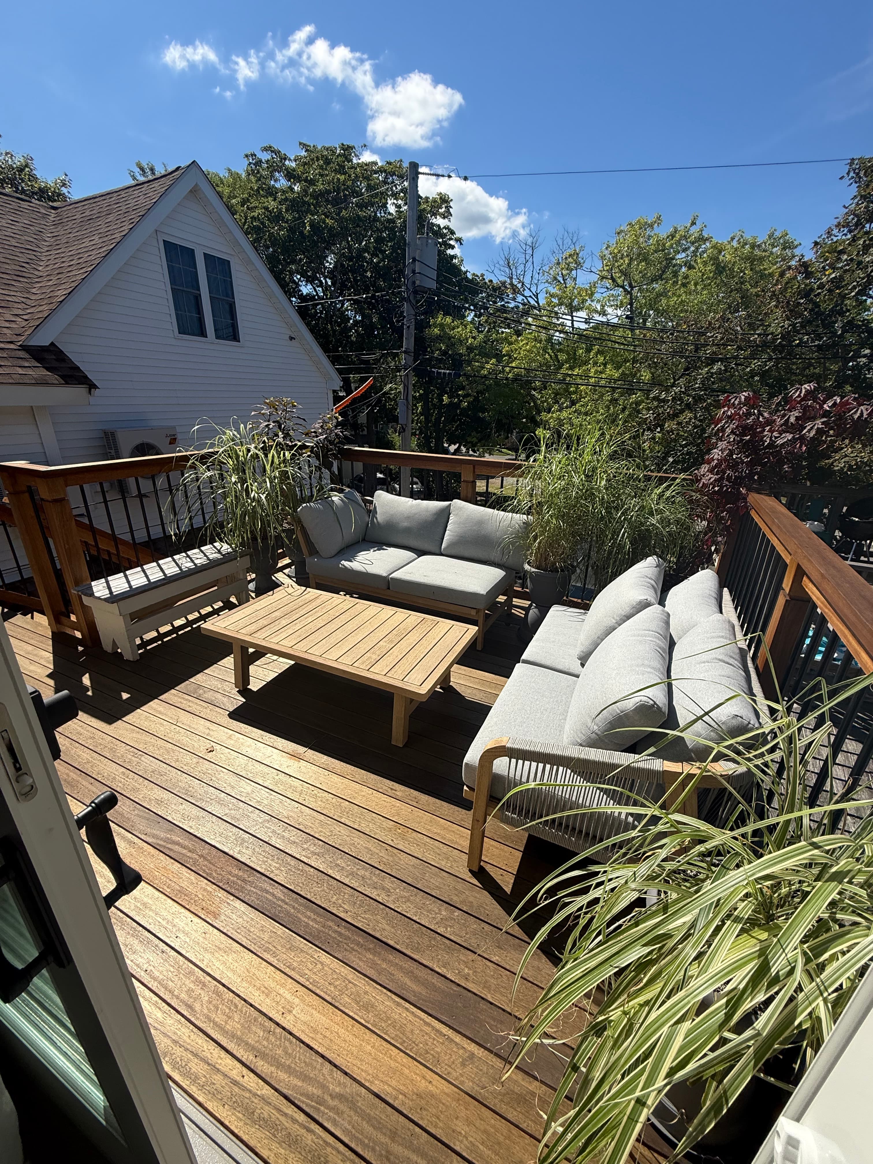 A cozy deck featuring a wooden table, gray seating, and decorative plants under a clear blue sky.
